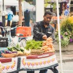 Homem organiza verduras frescas em uma banca de feira ao ar livre.