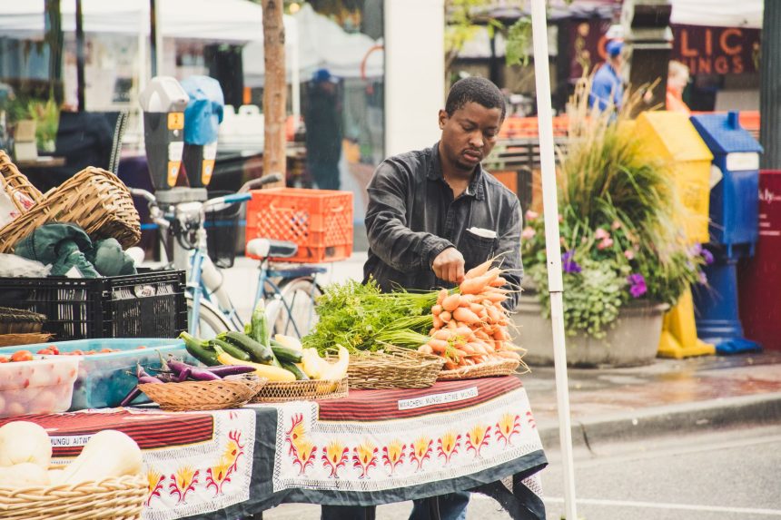 Homem organiza verduras frescas em uma banca de feira ao ar livre.
