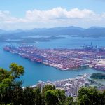 Vista aérea de um porto industrial com navios e contêineres em uma área costeira.