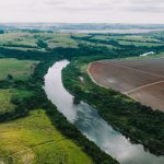 Áreas agrícolas às margens de um rio, sob céu parcialmente nublado, em paisagem rural de São Paulo.