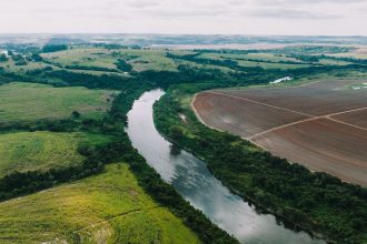 Áreas agrícolas às margens de um rio, sob céu parcialmente nublado, em paisagem rural de São Paulo.