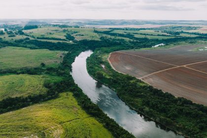Áreas agrícolas às margens de um rio, sob céu parcialmente nublado, em paisagem rural de São Paulo.