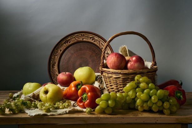 Composição de maçãs, uvas e peras, acompanhadas de outros produtos agrícolas, dispostas sobre uma superfície rústica.