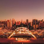 Vista aérea de Maringá ao entardecer, com edifícios, o terminal intermodal e a área urbana do município.