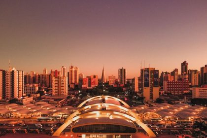 Vista aérea de Maringá ao entardecer, com edifícios, o terminal intermodal e a área urbana do município.