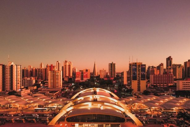 Vista aérea de Maringá ao entardecer, com edifícios, o terminal intermodal e a área urbana do município.