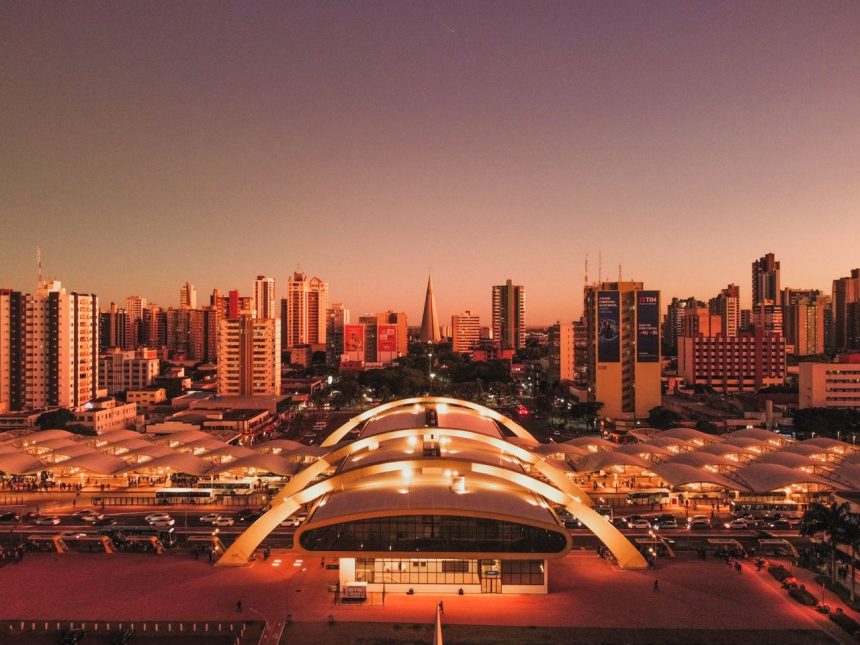 Vista aérea de Maringá ao entardecer, com edifícios, o terminal intermodal e a área urbana do município.