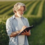 Agricultor em uma lavoura verde faz anotações em uma prancheta enquanto avalia a produção.