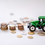 Miniatura de trator verde ao lado de pilhas de moedas sobre uma superfície.