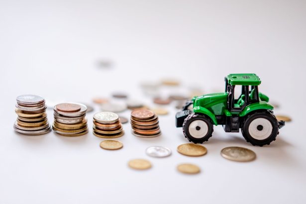 Miniatura de trator verde ao lado de pilhas de moedas sobre uma superfície.