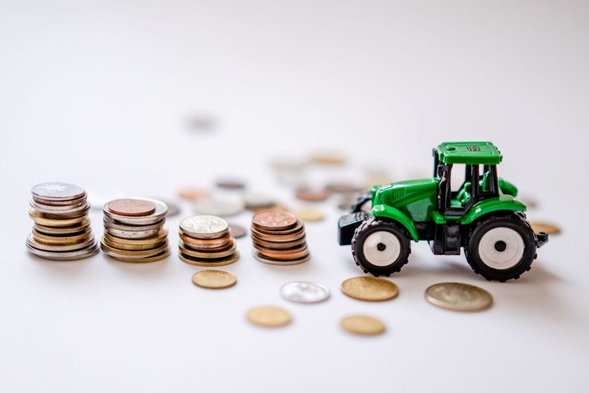 Miniatura de trator verde ao lado de pilhas de moedas sobre uma superfície.