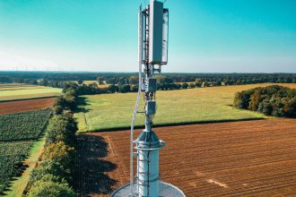 Torre de telefonia celular instalada em meio a áreas agrícolas vistas de cima.