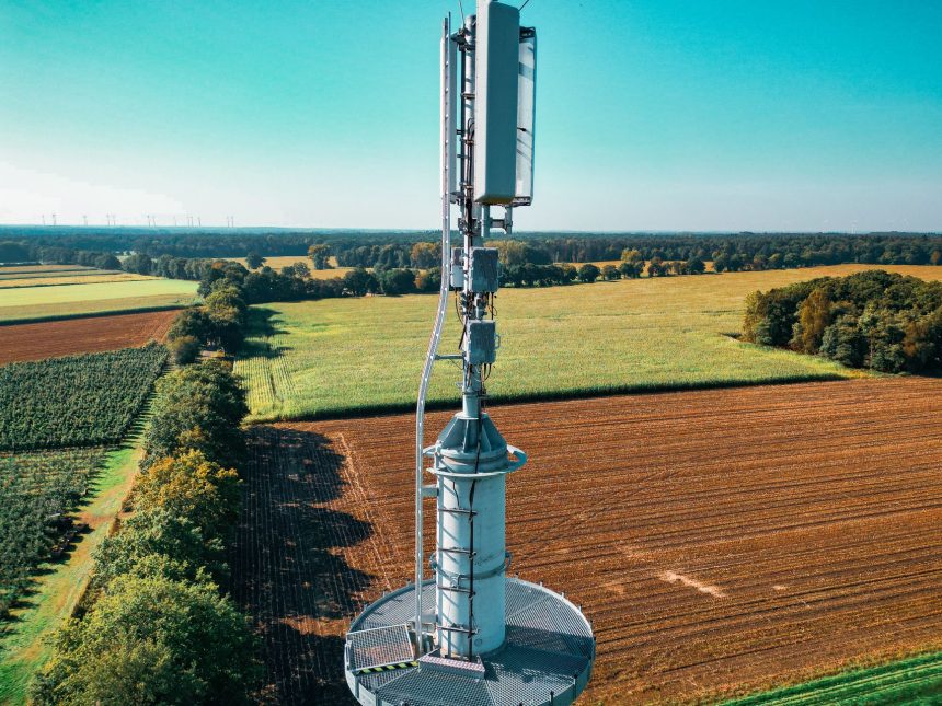 Torre de telefonia celular instalada em meio a áreas agrícolas vistas de cima.